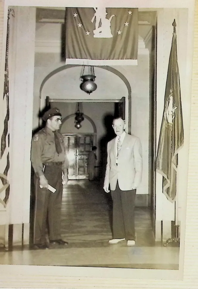 Officer Bull Curry in uniform standing with an official in a marble courthouse hall with flags