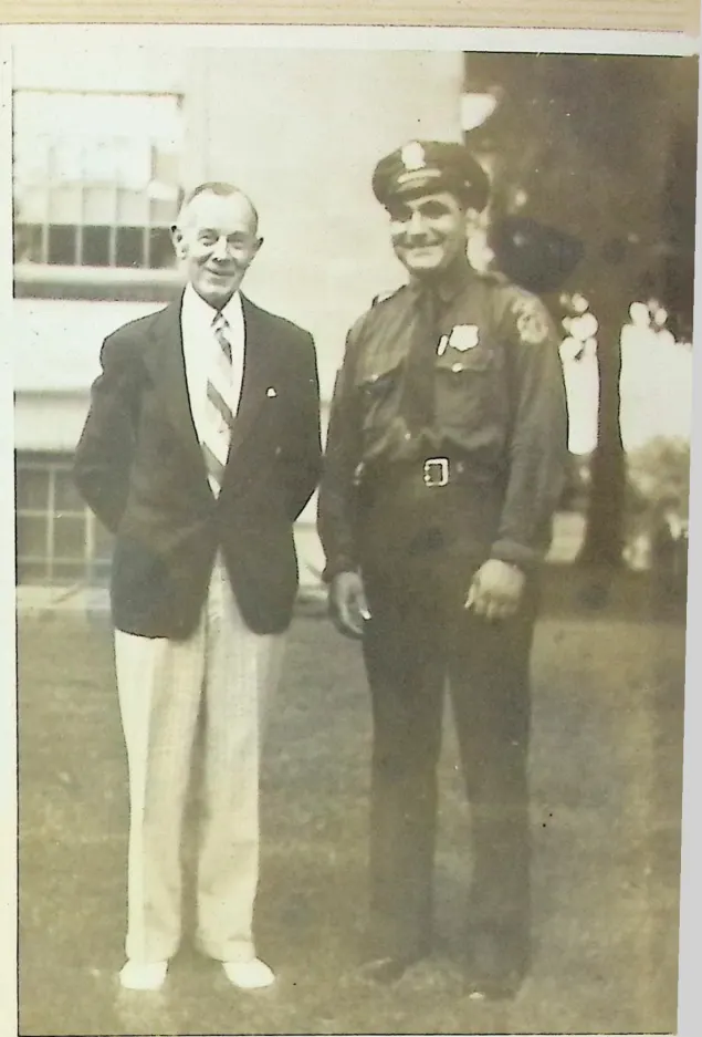 A young officer Bull Curry beaming in uniform beside an older man in a blazer on a lawn